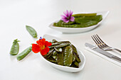 Delicious roasted snow peas garnished with flowers and served on plates near silverware on white table during lunch