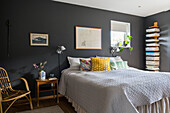 Queen bed in a bedroom with painting hung on the dark walls and vertical bookcase