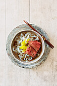 Vietnamese beef soup (Pho Bo) with bean sprouts, ribbon noodles, and slices of bison medallion