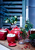 Rotes Geschirr und weihnachtlich dekorierte Flaschen als Kerzenhalter