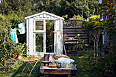 Greenhouse built from old windows, wooden day bed in front of it