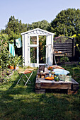 Greenhouse built from old windows, wooden day bed in front of it