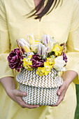 Woman in yellow dress holds a basket of colorful spring flowers