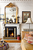 Mirror with gilded frame on a mantelpiece, in the foreground sofa with floor cushion