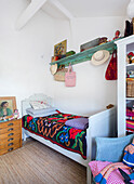 Bed with colourful bedspread, above it green shelf in white painted guest room