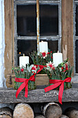 Christmas candle decoration with red bows on a wooden bench in front of a window