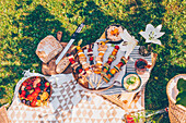 A picnic in a garden: vegetarian sandwich kebabs, bread, dips and a bowl of fresh summer fruits