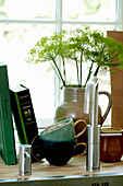 Tassen, Bücher und Vase mit Dillblüte vor Küchenfenster