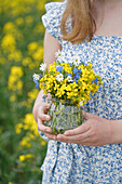 Woman holding a bouquet of wild flowers in a glass vase against a background of yellow flowers