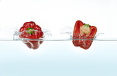 Two red peppers splashing in water