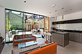 Orange upholstered sofas with animal-print cushions and a modern fitted kitchen in open-plan living area