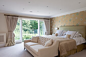 Doppelbett mit hohem Betthaupt vor Wand mit Tapete und helles Sofa im Schlafzimmer