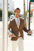 A laughing young business man wearing a brown jecket and light trousers on the street