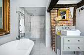 Frei stehende Badewanne, Kommode mit Waschbecken, im Hintergrund Duschbereich in hellgrauem Bad