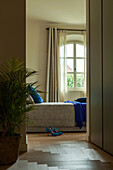 Blick ins Schlafzimmer mit grauer Tagesdecke und blauem Überwurf