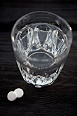 Two aspirin tablets next to a glass of water
