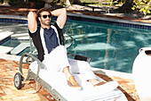 Young man with a beard in a polo shirt and white pants is sitting on a lounger
