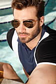 Junger Mann mit Bart und Sonnenbrille in Polo-Shirt am Pool