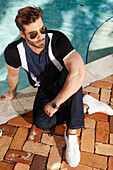 Young man with a beard and sunglasses sits on the edge of the pool