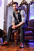 Elegant young man with beard sits on leather armchair