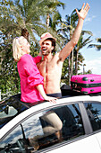 Cheerful couple in holiday spirit are standing in the roof window opening of a car