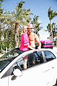 Cheerful couple in holiday spirit are standing in the roof window opening of a car