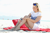 Junge blonde Frau in Freizeitbekleidung kühlt sich das Bein mit Eiswürfel am Strand