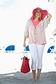 Junge blonde Frau mir pinkem Hut in Freizeitbekleidung am Strand