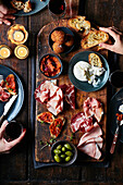Sharing platter of cold cured meats, burrata, olives and mini arancini with hands