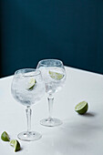 Two gin and tonics with ice cubes and lime wedges