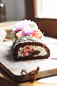 Erdbeer-Schokoladen-Biskuitrolle dekoriert mit Sahne und Blüten