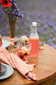 Waldbeeren-Limonade in Glas und Flasche auf Tisch im Freien