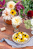 Blumenarrangement mit Dahlien, Rudbeckia und Margeriten auf Gartentisch