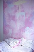 Bett im Schlafzimmer mit individueller Wandgestaltung in rosa Tönen