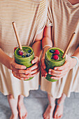 Hands holding two green smoothies