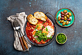Shakshouka made of eggs and tomato sauce served in pan with toasts, fresh cilantro and olives (Middle Eastern and Maghrebi)