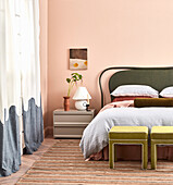 Doppelbett mit Betthaupt und zwei Polsterhocker in hohem Raum mit rosa Wänden