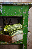Frische Zucchini in Holzkiste unter grünem Holztisch