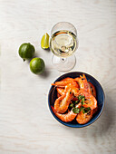 Boiled prawns in a bowl next to a glass of white wine and limes