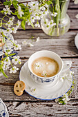 Kaffee serviert mit einem Keks umgeben von Frühlingsblumen