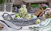 Kräuterbutter in Eiform mit Schnittlauch, Petersilie, Knoblauch, Thymian, dekoriert mit Gänseblümchen auf Silbertablett