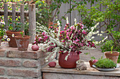 Blumenstrauß aus Brautspiere (Spiraea x arguta), Tulpen (Tulipa) und Zierapfel in Tonkrug und Osterdeko auf Terrasse
