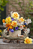 Blumenvase mit Kronen-Anemone (Anemone coronaria), Narzissen (Narcissus), Primeln, Felsenbirnen (Amelanchier) auf Holzscheibe