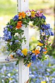 Flower wreath with daisies, hyacinths, dandelions, grape hyacinths, oregano, thyme, forget-me-nots, violets and garden pansies (Viola wittrockiana)