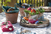 Easter eggs with cress in glasses on wooden disc, bread slices in clay pots and cutlery on table, Easter decoration