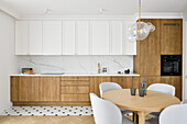 Fitted kitchen with white wall unit and wooden cabinet fronts, round dining table in the foreground
