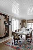 Dining area with antique chairs, large painting with dress motif on wall