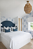 Double bed in bright, light-flooded bedroom with blue and white wallpaper