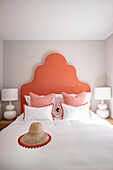 Double bed with generous, coral-coloured headboard, flanked by bedside tables with white lamps