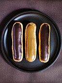 Eclairs mit Schokoladen- und Karamellglasur auf schwarzem Teller